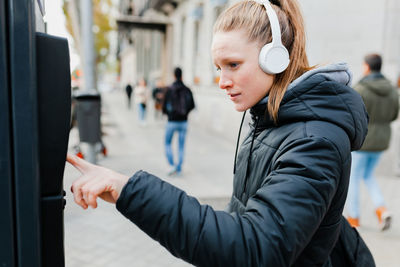 Young woman listening to music using parking meter