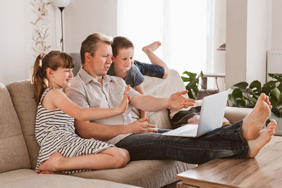 Video call. dad and children sit on the couch and call online grandparents or mom. communication