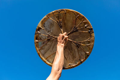 Low angle view of person holding umbrella against clear blue sky