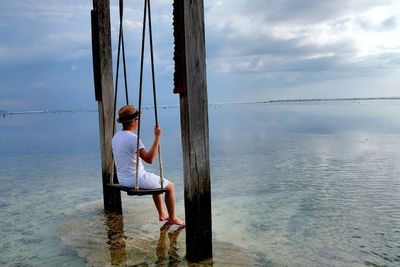 Woman sitting on swing against sea at beach