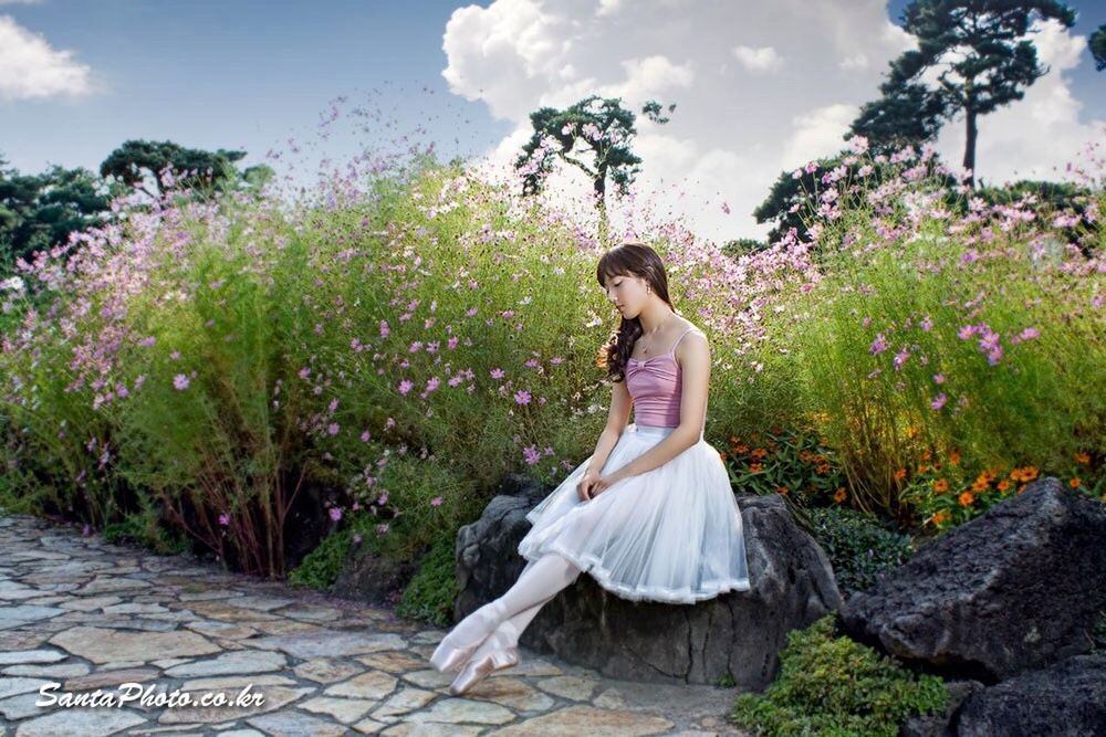 tree, sky, full length, casual clothing, lifestyles, growth, plant, leisure activity, sitting, flower, cloud - sky, nature, relaxation, day, young adult, standing, outdoors, young women