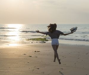 Rear view full length of woman with arms outstretched jumping at beach during sunset
