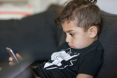 Boy using smart phone while reclining on sofa at home
