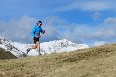 A man trains for ultra run trail on hilly meadow in autumn with the first snow on the mountains