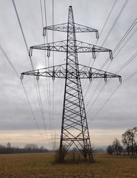 Low angle view of electricity pylon on field against sky