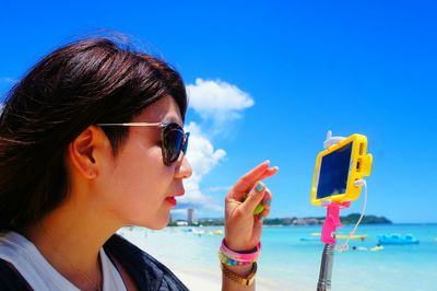 Close-up of young woman photographing with mobile phone at beach against sky