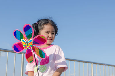 Girl holding pinwheel toy while standing on road against sky