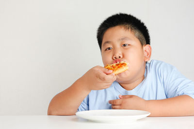 Portrait of boy eating food against white background