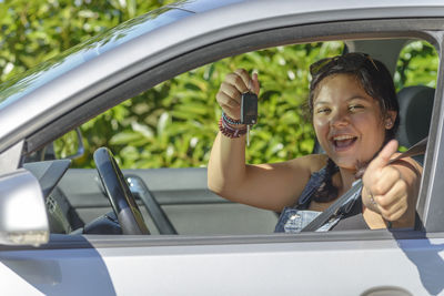 Portrait of happy woman holding key while gesturing in car