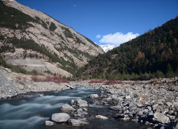 Scenic view of river by mountains against blue sky