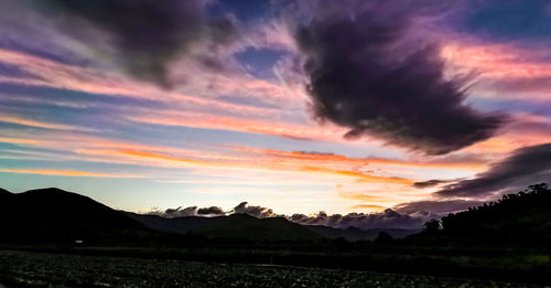 Scenic view of dramatic sky over silhouette landscape during sunset