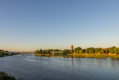 Scenic view of river by building against clear blue sky