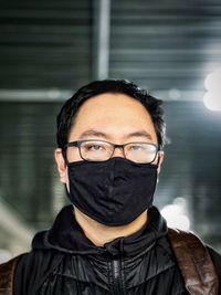 Portrait of man wearing eyeglasses and black face mask against ceiling.