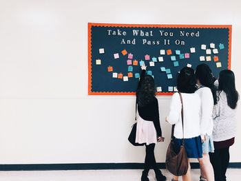 Rear view of students pointing at sticky notes in university corridor