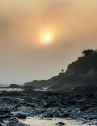 Distant view of silhouette surfer standing on mountain during sunset