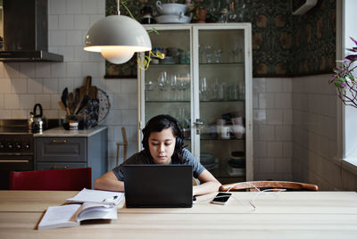 Serious boy wearing headphones while using laptop during homework at home