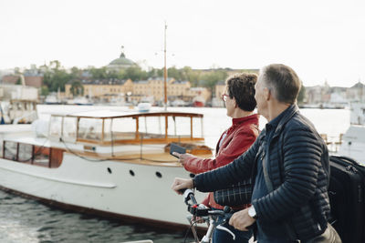 Senior couple with bicycle walking by harbor in city during vacation