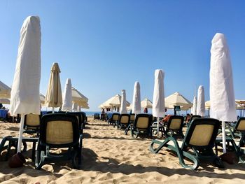 Lounge chairs and covered parasols at beach against clear sky