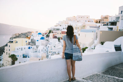 Greece, santorini, oia, back view of woman looking to the village at evening twilight