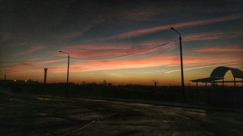 Empty road along silhouette landscape at sunset