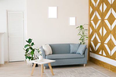 A dusty blue sofa with pillows, a white coffee table, potted plants in a bright cozy living room