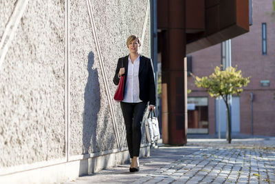Full length of businesswoman standing on footpath in city