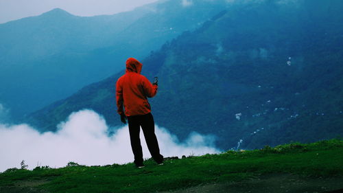 Rear view of man using phone while standing on mountain