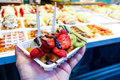 Cropped hand of person holding waffle and fruits in container at shop