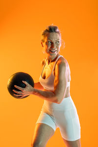 Portrait of young woman with arms raised standing against yellow background
