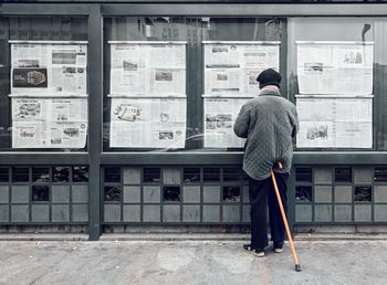 Rear view of mature man reading newspaper while standing on street