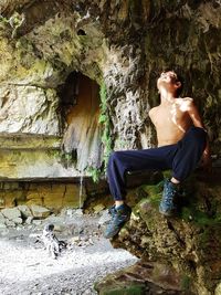 Full length of shirtless young woman sitting in cave