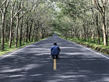 Rear view of man crouching on road amidst trees