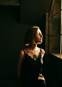 Young woman looking away while standing against wall