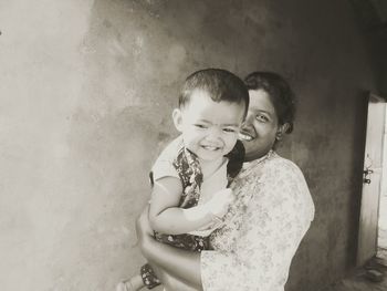 Portrait of smiling mother carrying daughter by wall