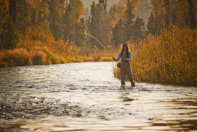 Woman fishing in river against plants at sunset