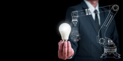 Midsection of man holding illuminated lighting equipment against black background