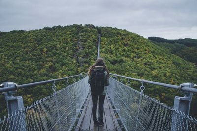 Rear view full length of woman standing on footbridge at forest