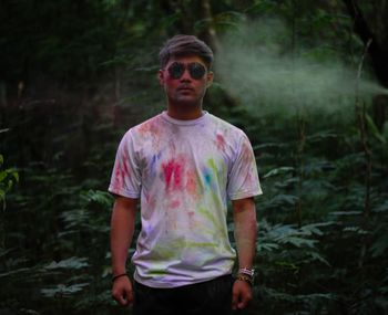 Portrait of young man wearing sunglasses standing in forest