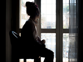 Side view of woman sitting against window