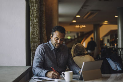 Male freelancer writing in diary while sitting with laptop at table