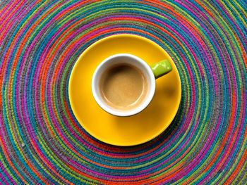 Directly above shot of coffee cup in plate on colorful tablecloth