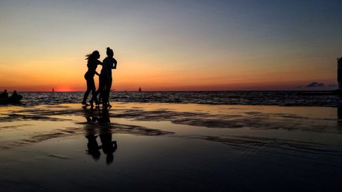 Silhouette friends on beach against sky during sunset