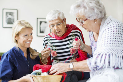 Happy female caretaker looking at senior women choosing wool for knitting at nursing home