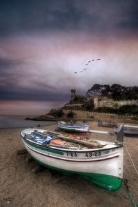 Boats moored on beach against sky during sunset