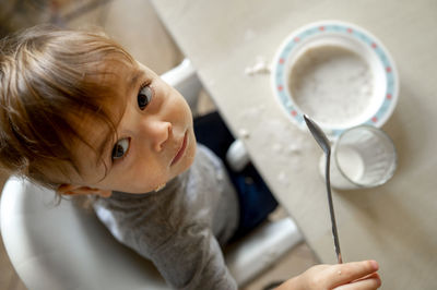 Baby boy with spoon having breakfast at table