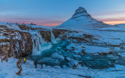 Scenic view of snow covered mountain and frozen waterfall against soft sunrise sky