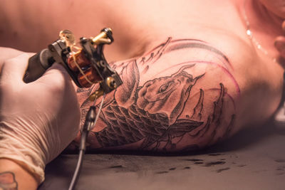 Cropped image of artist tattooing on customer body part