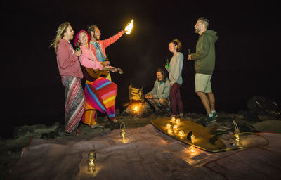 Friends standing by illuminated lighting equipment while camping at night