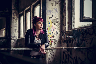 Woman looking away standing by railing in abandoned building