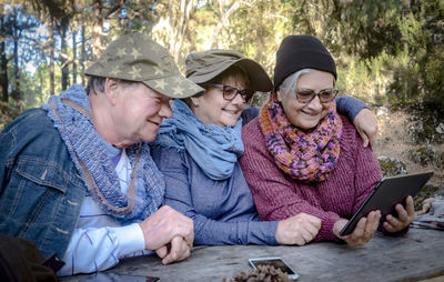 Senior people using digital tablet sitting on bench outdoors